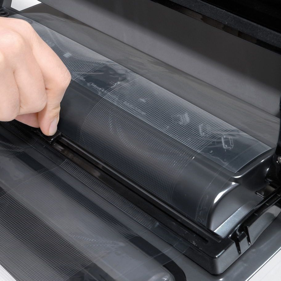 Nahaufnahme einer Hand, die einen Vakuumierer bedient, mit transparentem Kunststoff.