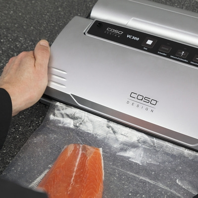 Person bedient Vakuumiergerät mit Lachs in Plastikbeutel. Caso VC300.
