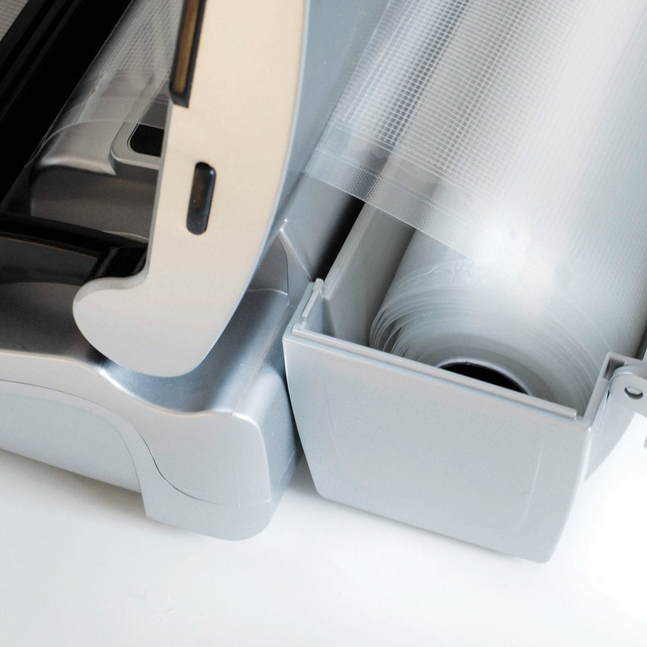 Nahaufnahme eines silbernen Vakuumiergeräts mit einer Rolle Plastikfolie.