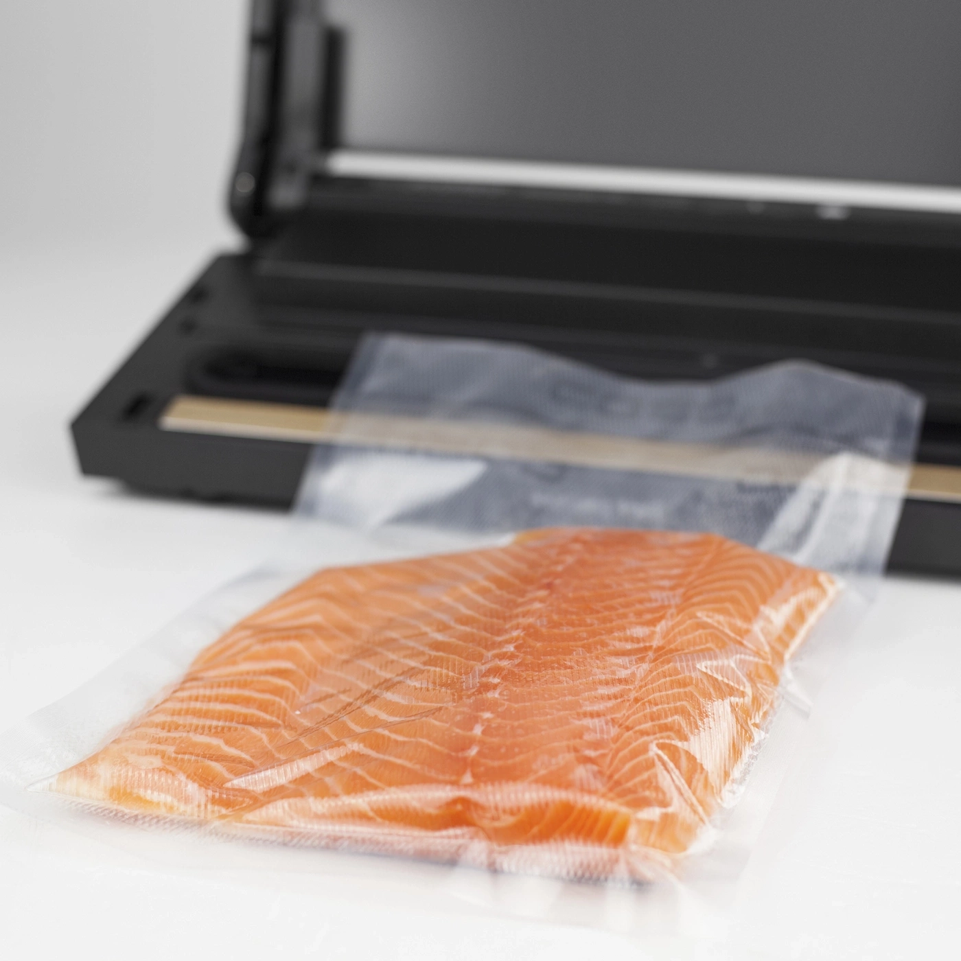 Lachsfilet in Vakuumverpackung vor Vakuumiergerät auf weißem Hintergrund